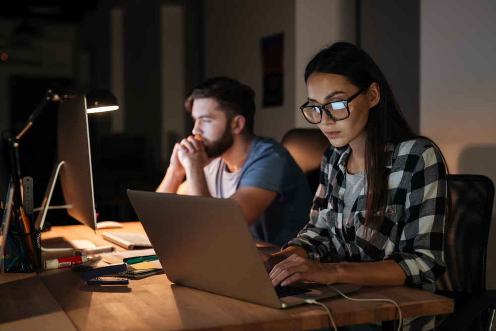 two-people-sitting-at-desk-side-by-side-looking-computers-how-business-coaching-software-help-confidence-potentia-blog-image